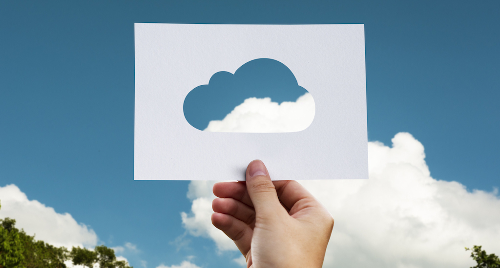 Hand holding paper cloud up in front of real clouds