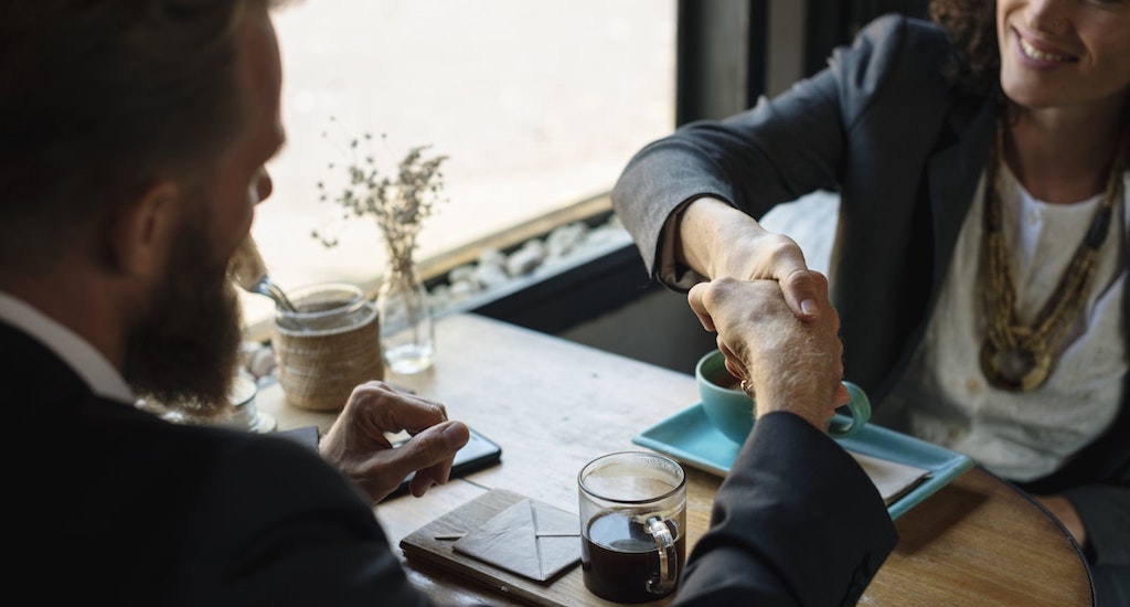 Two business people shaking hands over coffee table